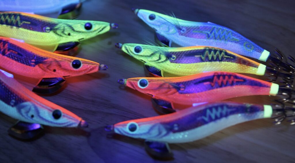 Yamashita EGI-OH Search Shallow squid jigs glowing under UV light showing the Neon Bright reflection colours